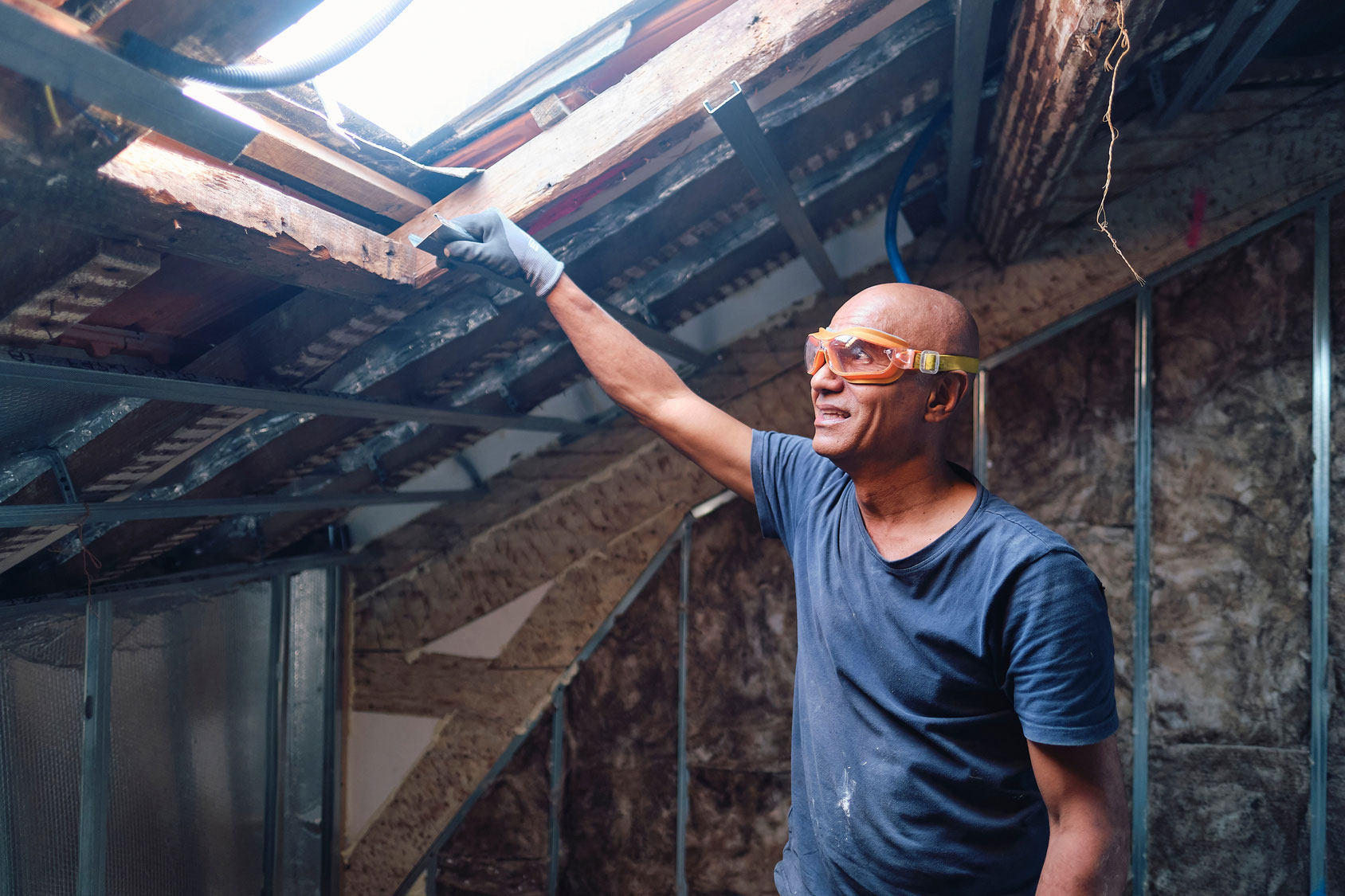 Man wearing protective safety glasses in a partially demolished construction building smiles out a skylight overhead.